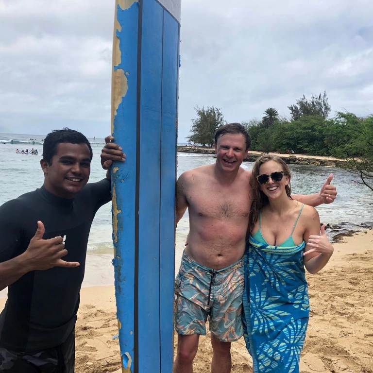 Local guide Kala Grace standing on the beach with a couple and their surfboard after completing couples surf lessons.