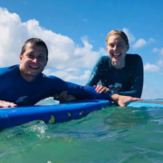 A happy couple enjoying a surf date while sitting on a longboard in the clear blue water at Puaena Point, Oahu.